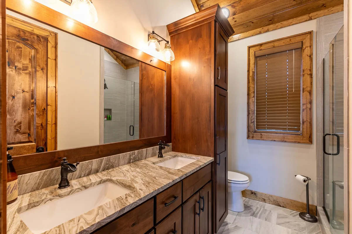 A serene en-suite bathroom featuring a double sink vanity, large mirror, walk-in shower, and wooden cabinetry. The space is designed for calm and privacy, ideal for unwinding after a day of adventure.