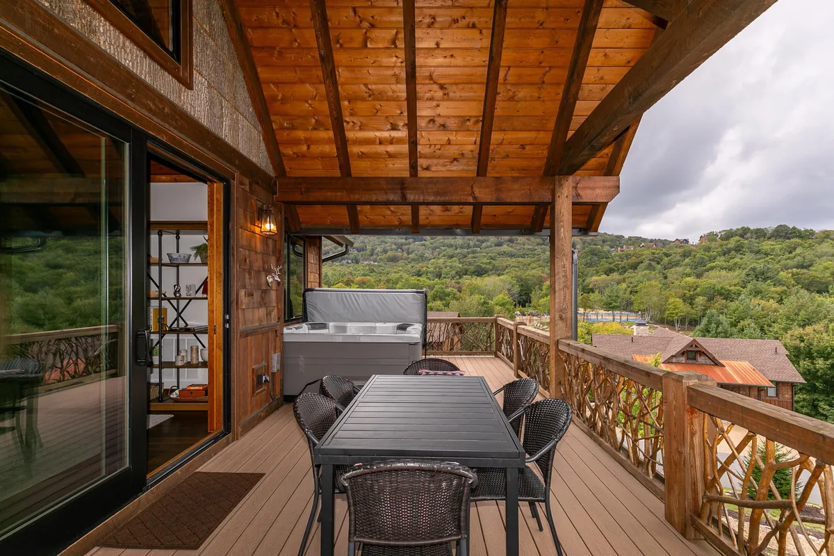 This image showcases a spacious wooden deck featuring a private hot tub, an outdoor dining table, and beautiful surrounding greenery. The inviting setup highlights a spot ideal for both relaxation and entertaining guests while offering unobstructed mountain views.