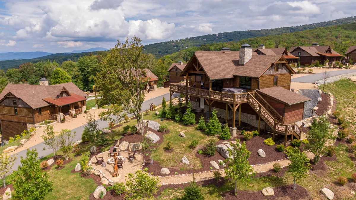 An exterior scene featuring the main lodge, surrounding cabins, and a landscaped garden with a pathway. The communal layout and green spaces evoke a welcoming, community-oriented atmosphere ideal for families and pets alike.