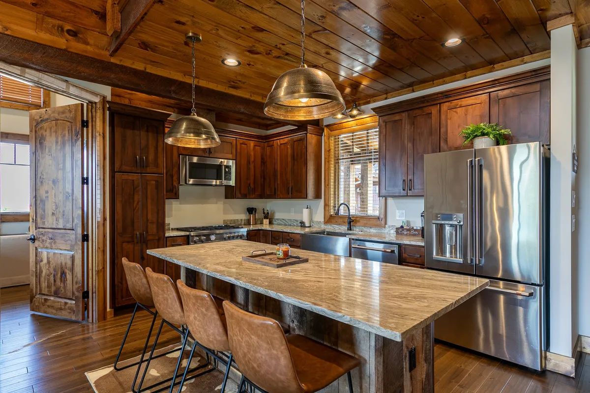 A closer look at the modern kitchen area, featuring a spacious kitchen island, copper pendant lighting, wooden cabinetry, and stainless steel appliances. The design is both functional and inviting, ideal for preparing hearty breakfasts or special dinners with a picturesque backdrop.