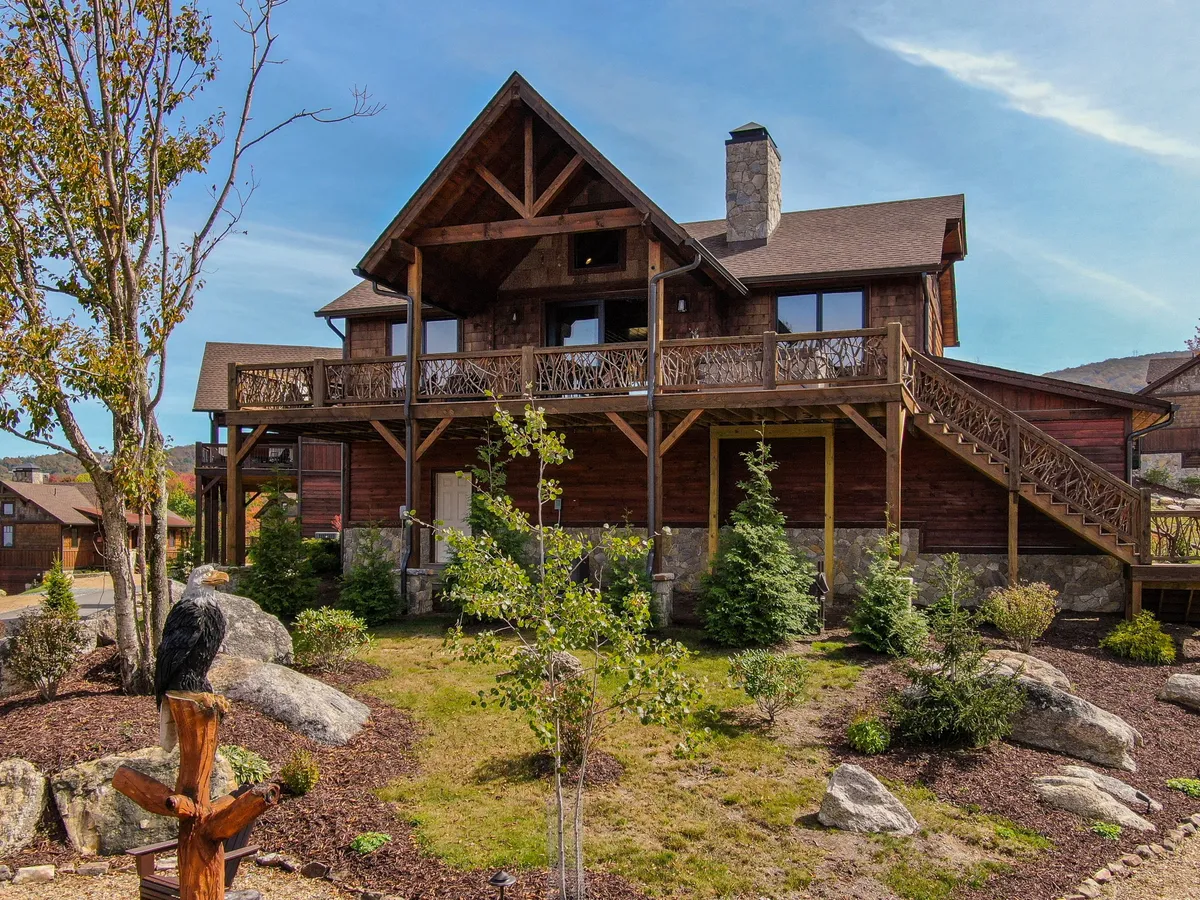This image features a large wooden balcony overlooking a landscaped garden adorned with rocks and decorative railing. The balcony is attached to a cozy mountain home with a visible stone chimney, and the surrounding garden is lush and inviting, suggesting direct access to nature and tranquil outdoor living.