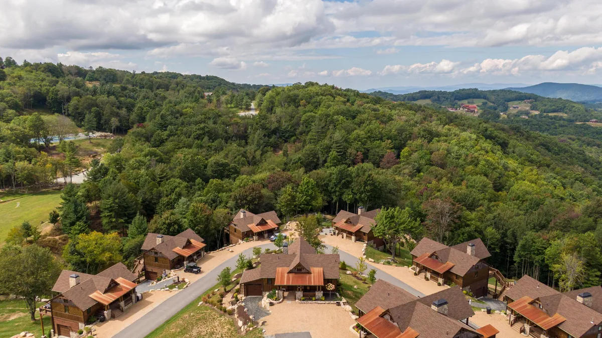 A scenic view of a cluster of cabins nestled in forested hills, connected by a winding road. The communal arrangement suggests plenty of space for groups, set within a peaceful, natural environment. The image hints at exploration and group adventure possibilities.