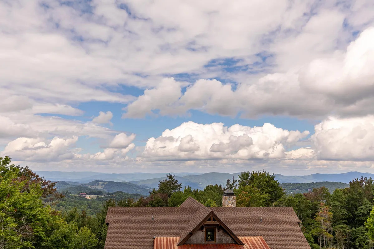 A wide, tranquil view of a mountain range under soft clouds, with part of a roof structure suggesting proximity to the retreat. The scene evokes feelings of adventure and immersion in nature, perfect for hiking and exploration.