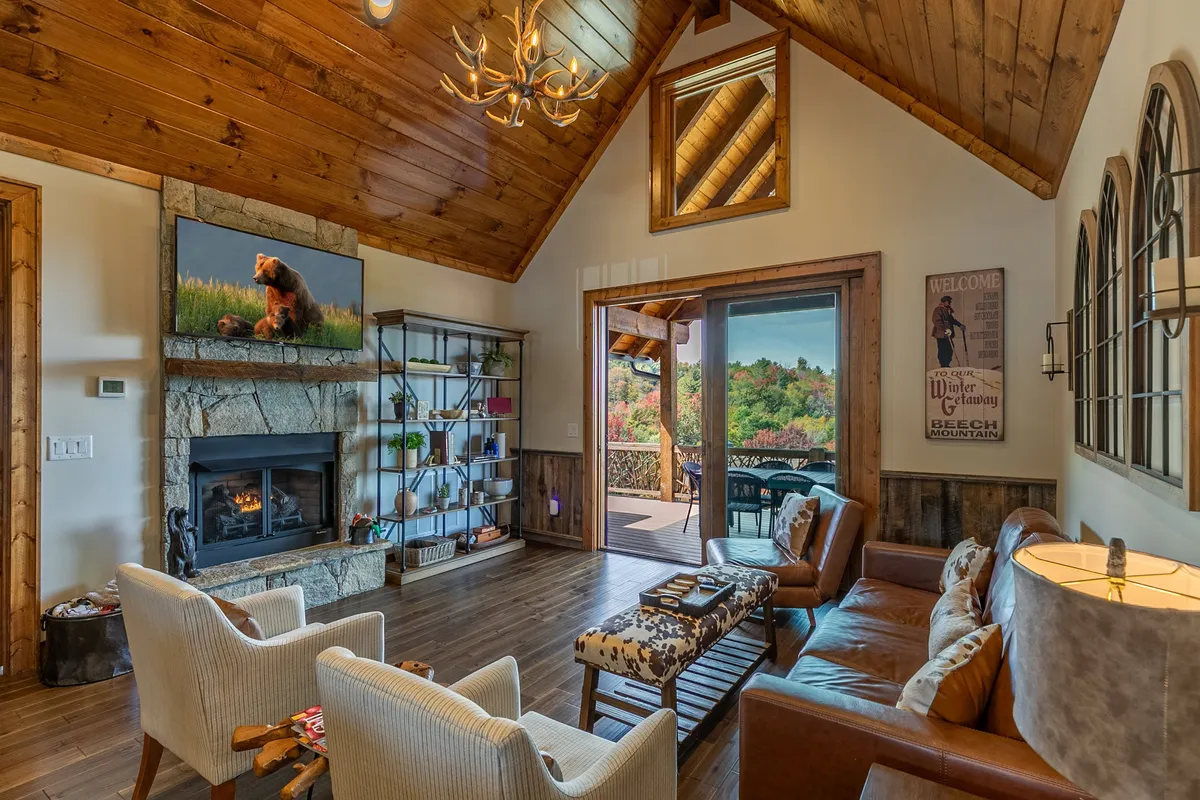 A warm and inviting living room with a gas log fireplace as the central feature. Comfortable sofas are arranged to create an intimate seating area, accented by decorative bear artwork on the wall. Large windows reveal mountain views and fill the space with natural light, while a Smart TV is conveniently positioned for movie nights or streaming entertainment.