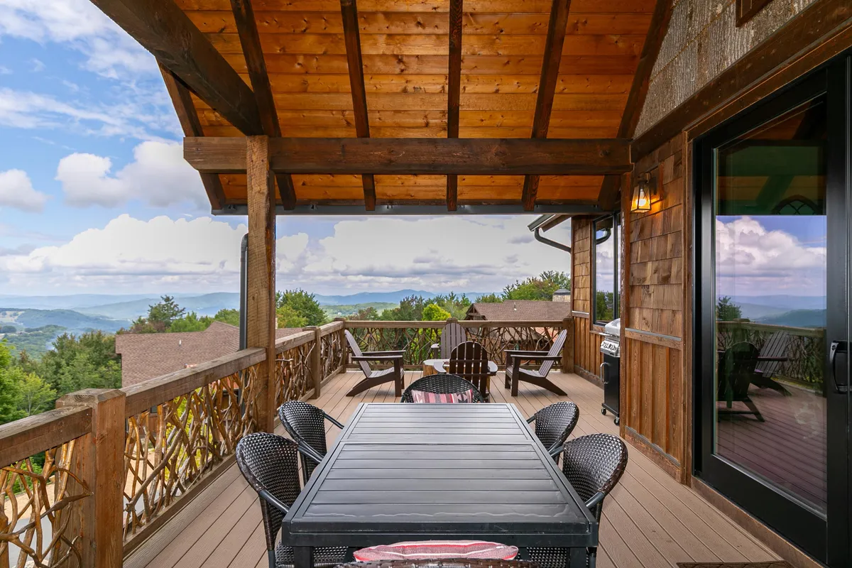 A spacious wooden deck furnished with an outdoor dining table and Adirondack chairs, all overlooking expansive mountain vistas. The scene radiates tranquility and invites relaxation or group activities like grilling and dining together after a day of adventure.