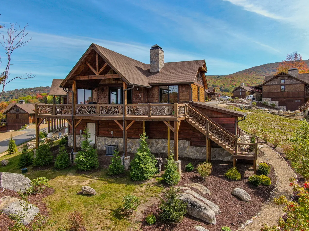 This exterior shot highlights a wooden balcony and stone chimney, surrounded by well-kept landscaping. The space feels open and inviting, set against the backdrop of a serene mountain landscape. The balcony and outdoor area are perfect for pets to enjoy fresh air while being safely contained.